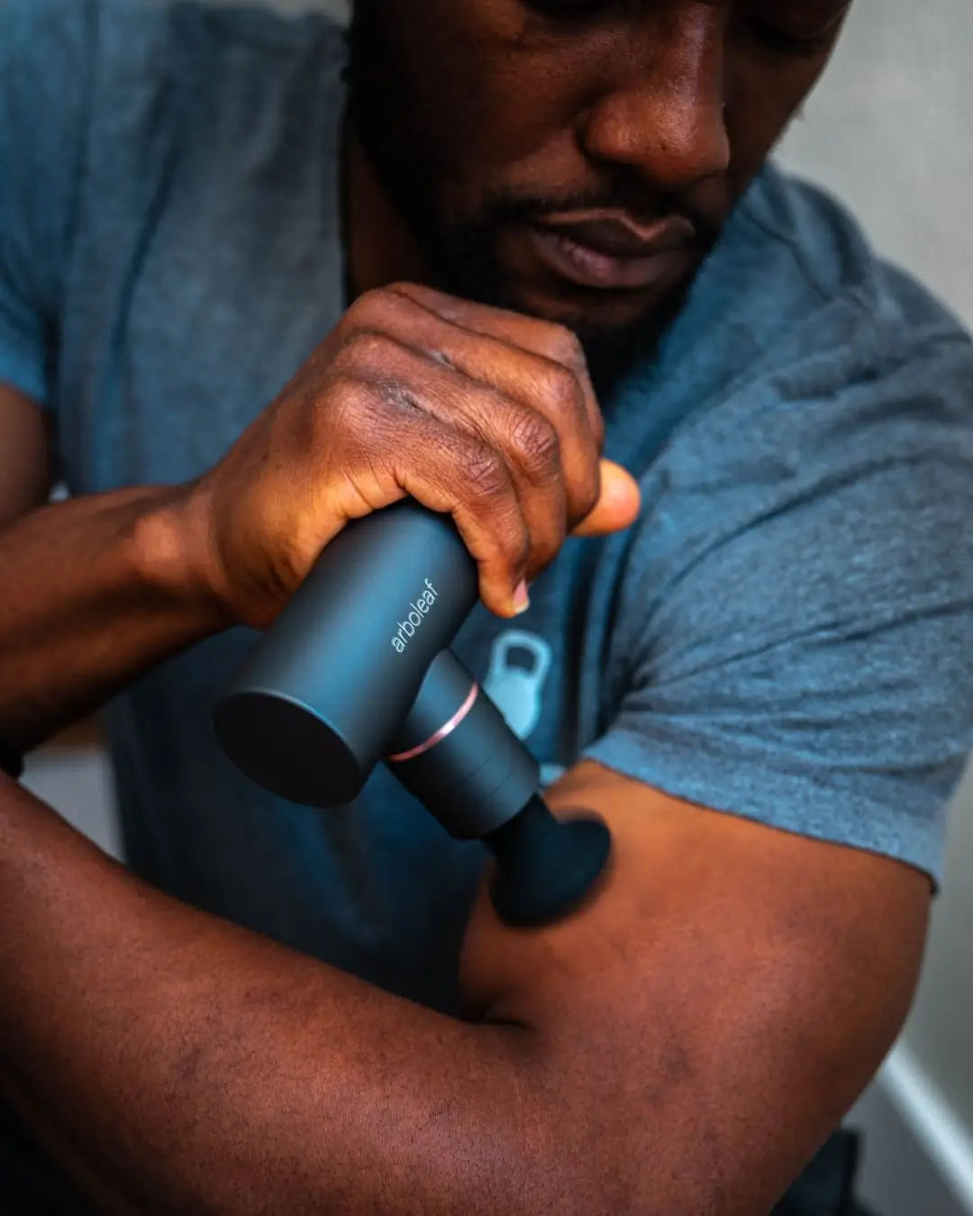man using Arboleaf massage gun to massage arm muscles