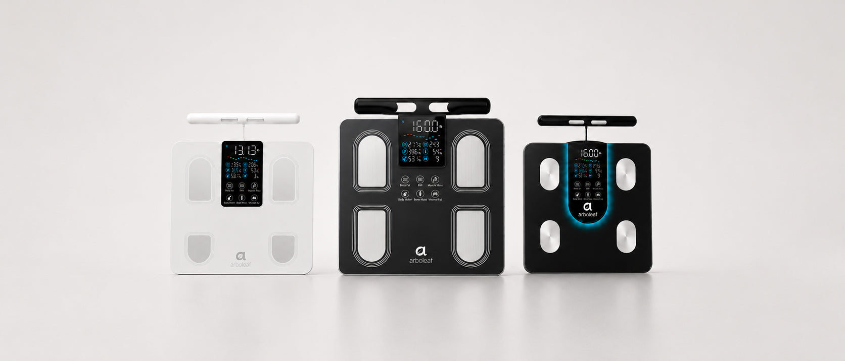 Three digital body composition scales are displayed side-by-side against a clean white studio background. The left scale is white, the center scale is black, and the right scale is black with a blue accent border around the screen.